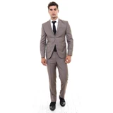 En mand i lysebrunt jakkesæt, hvid skjorte, sort slips og sorte sko står med front mod en hvid baggrund.